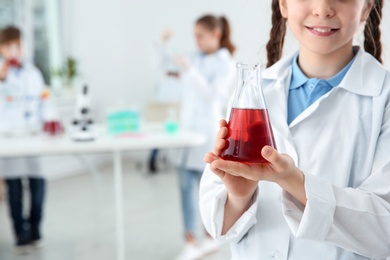Schoolgirl holding conical flask at chemistry class, closeup