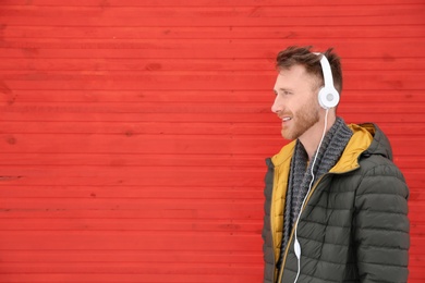 Young man listening to music with headphones against color wall. Space for text