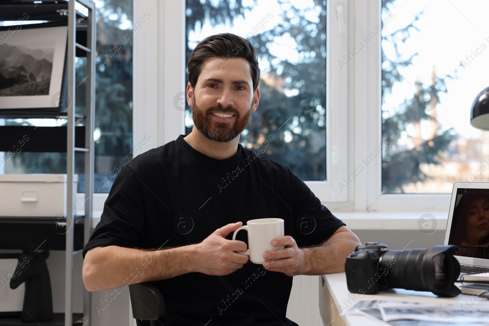 Photo of Professional photographer with cup of drink at table in office