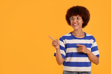 Photo of Happy young woman pointing at something on orange background. Space for text