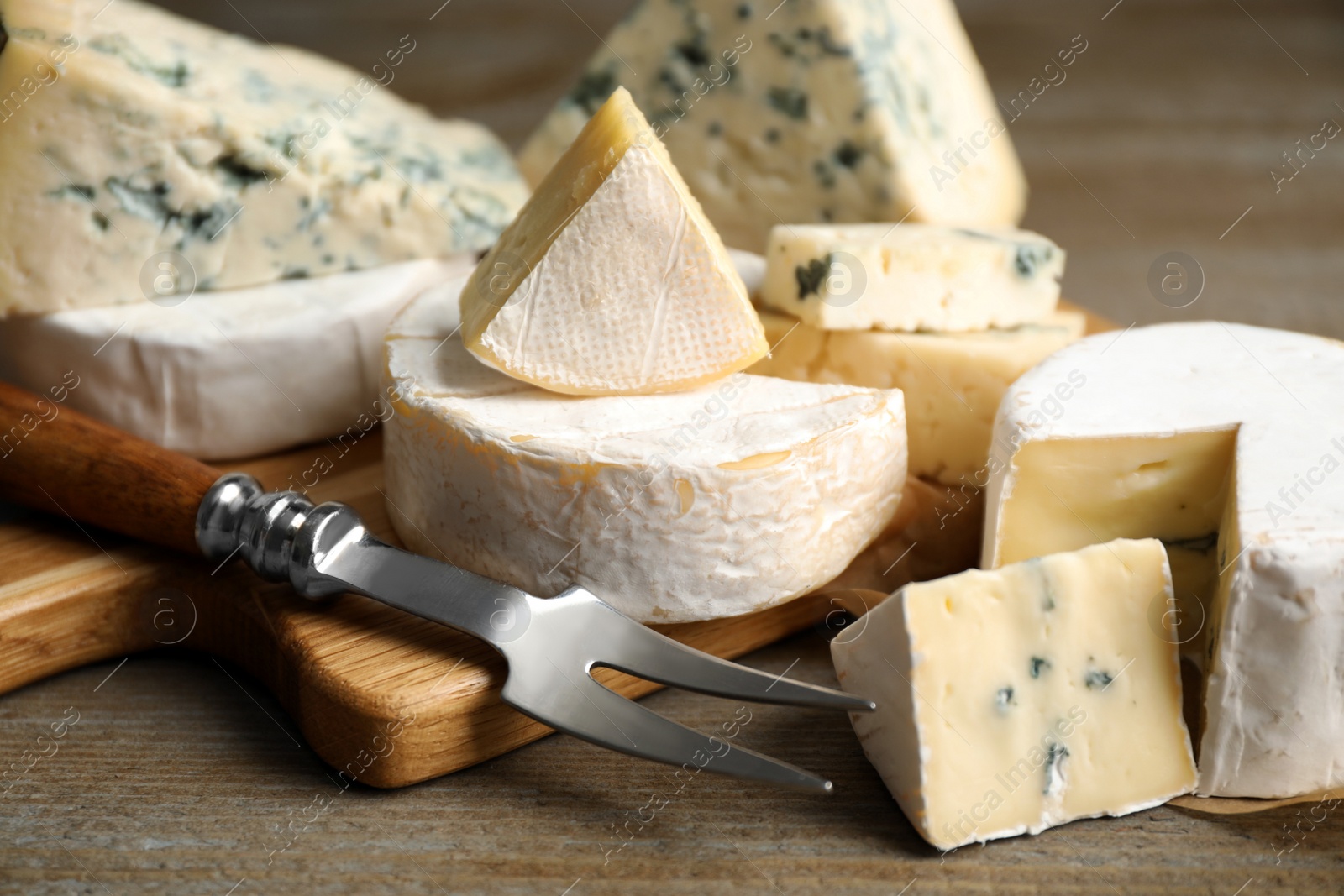 Photo of Different sorts of cheese and fork on wooden table, closeup