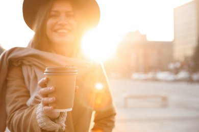 Young woman with cup of coffee on city street in morning, focus on hand