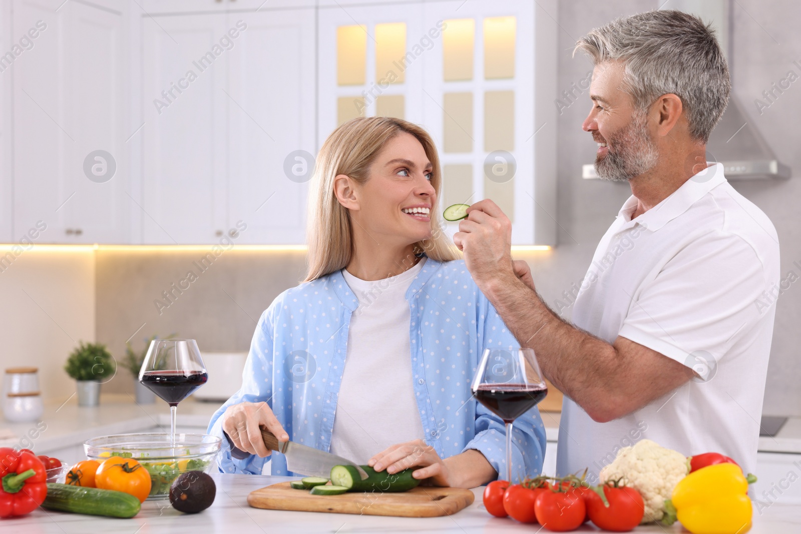 Photo of Happy affectionate couple cooking together at white table in kitchen