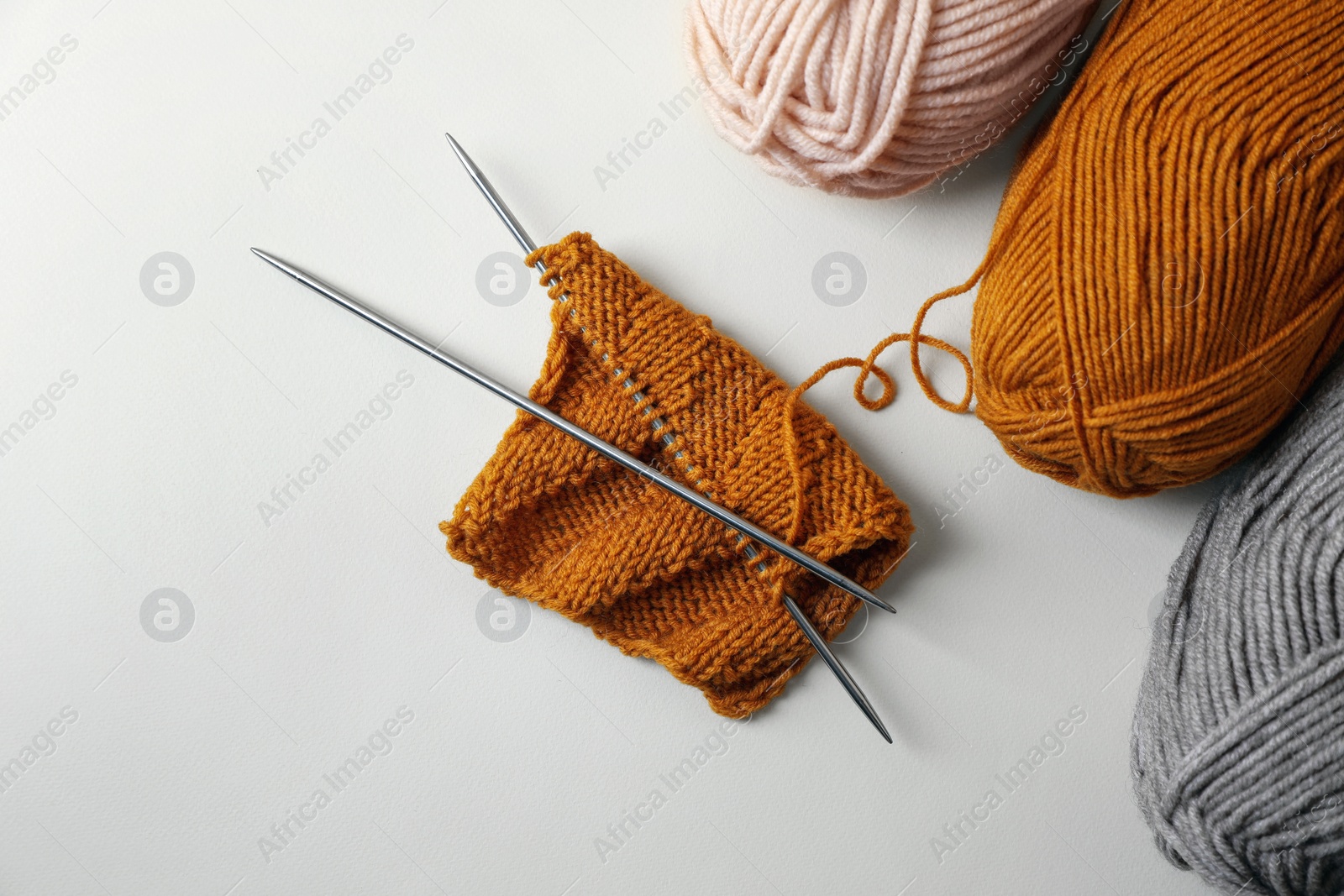 Photo of Soft colorful yarns, knitting and metal needles on beige background, flat lay