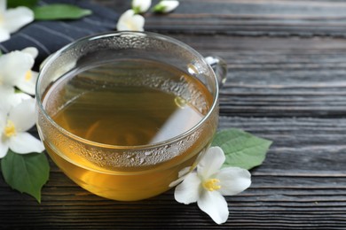 Photo of Cup of tea and fresh jasmine flowers on black wooden table