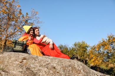 Photo of Couple of campers in sleeping bags sitting on rock. Space for text