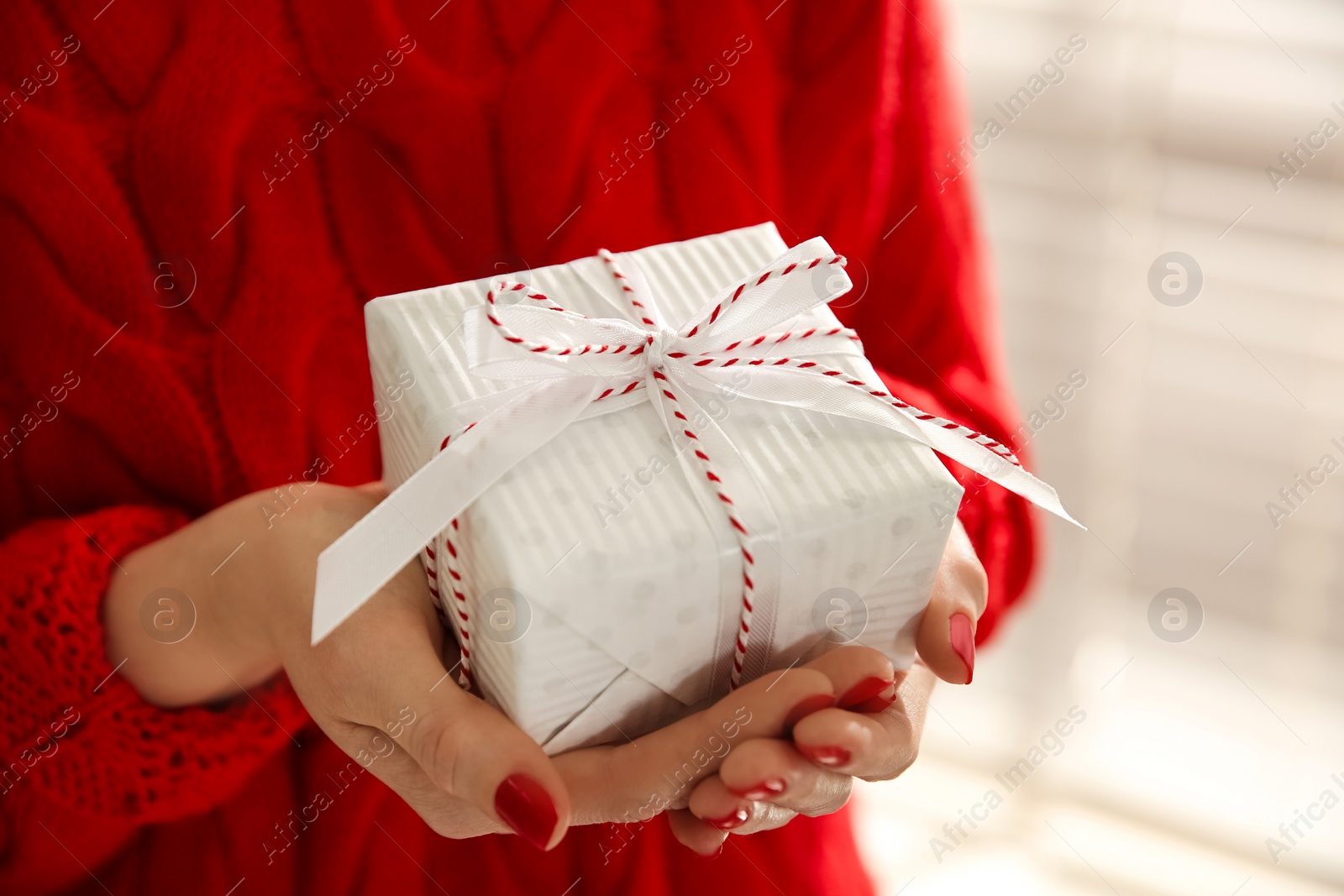 Photo of Woman holding white Christmas gift box indoors, closeup