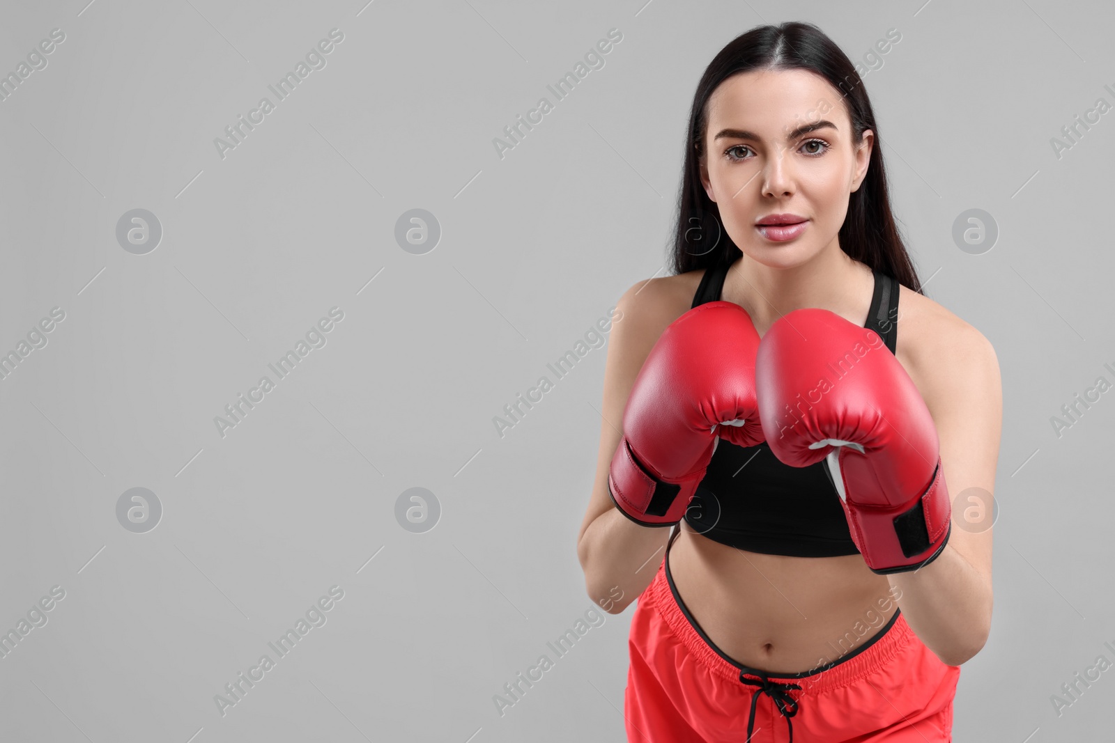 Photo of Portrait of beautiful woman in boxing gloves on grey background. Space for text