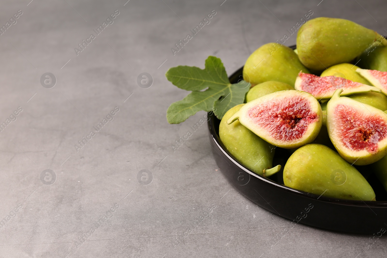 Photo of Cut and whole green figs on light gray table, closeup. Space for text