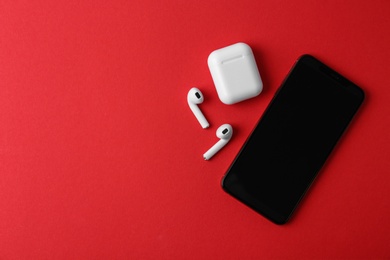 Photo of Wireless earphones, mobile phone and charging case on red background, flat lay. Space for text