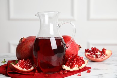 Photo of Pomegranate juice in jug and fresh fruits on white marble table, space for text