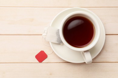 Photo of Tea bag and cup of hot beverage on light wooden table, top view