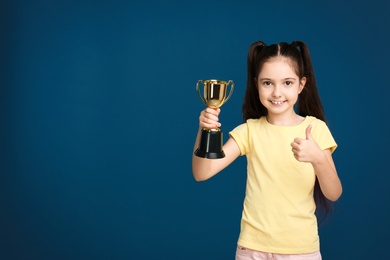 Photo of Happy girl with golden winning cup on dark blue background. Space for text