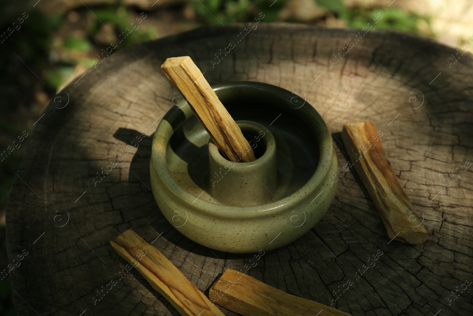 Photo of Palo santo sticks with holder on wooden stump outdoors