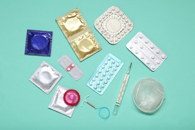 Photo of Contraceptive pills, condoms, intrauterine device and thermometer on turquoise background, flat lay. Different birth control methods
