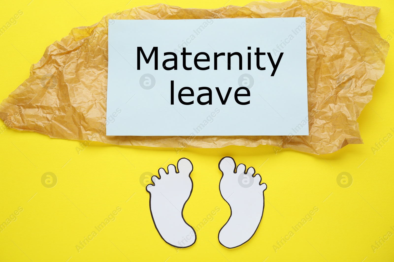 Photo of Note with words Maternity Leave and paper cutout of baby feet on yellow background, flat lay