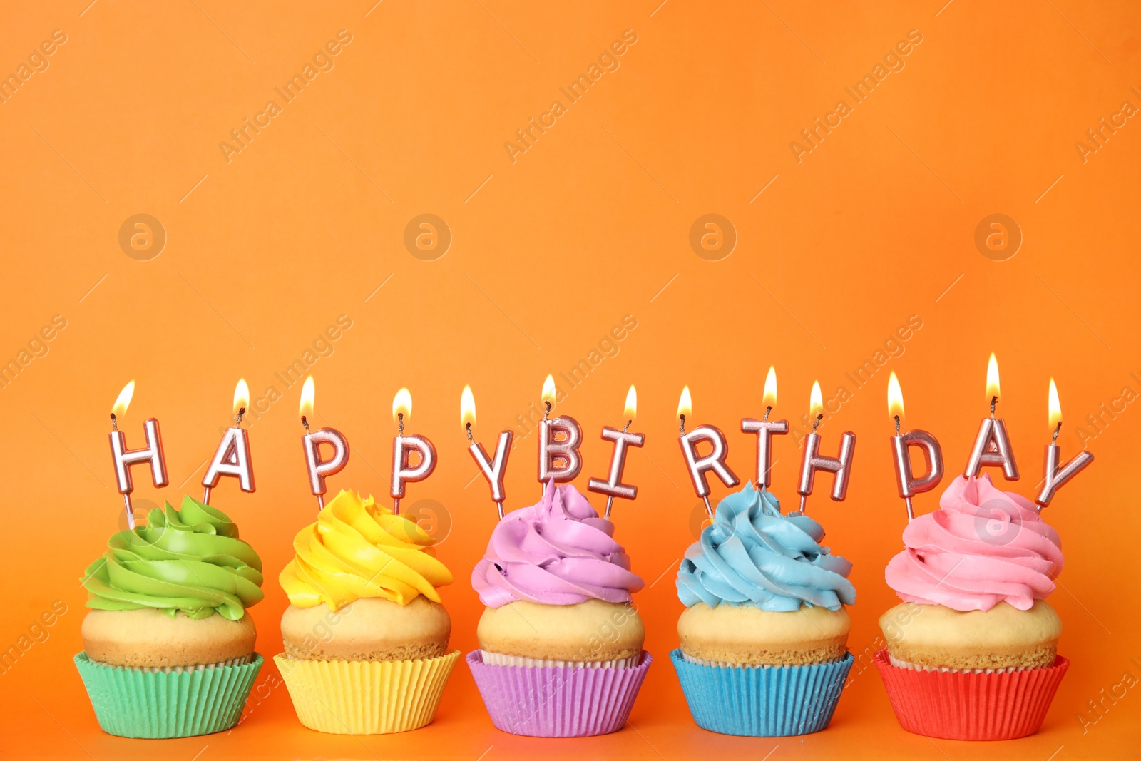 Photo of Birthday cupcakes with burning candles on orange background. Space for text