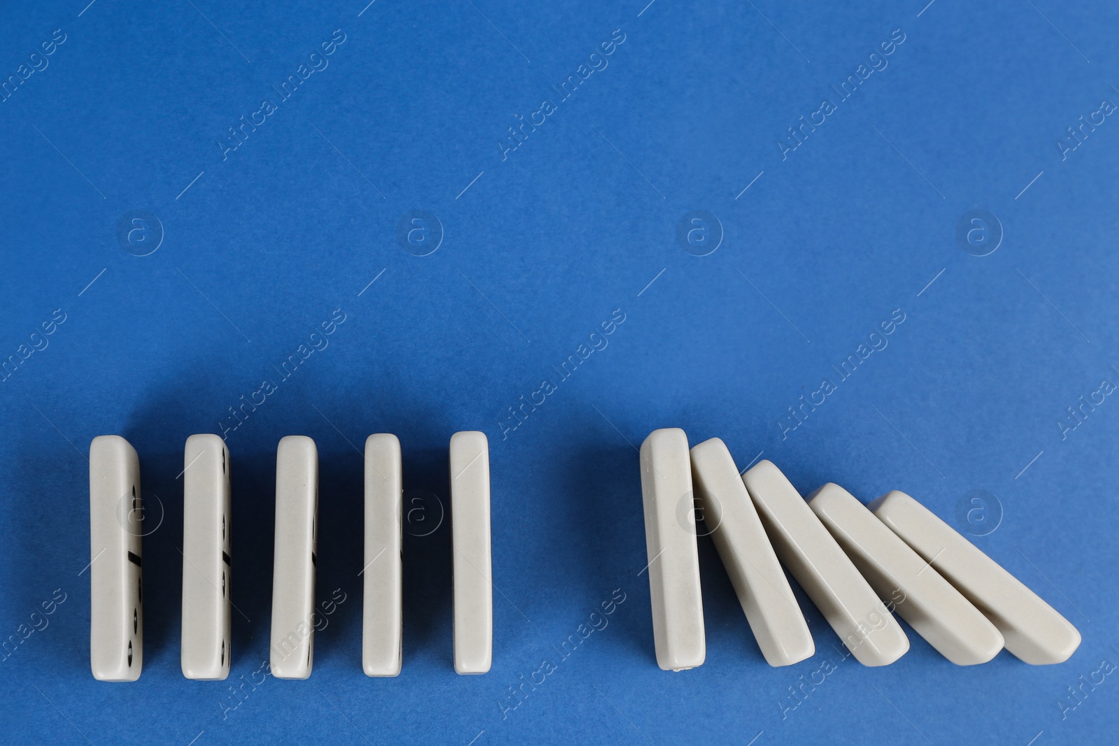 Photo of White domino tiles on blue background, flat lay. Space for text