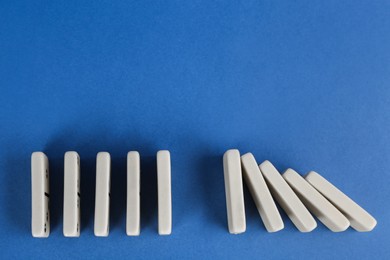 Photo of White domino tiles on blue background, flat lay. Space for text