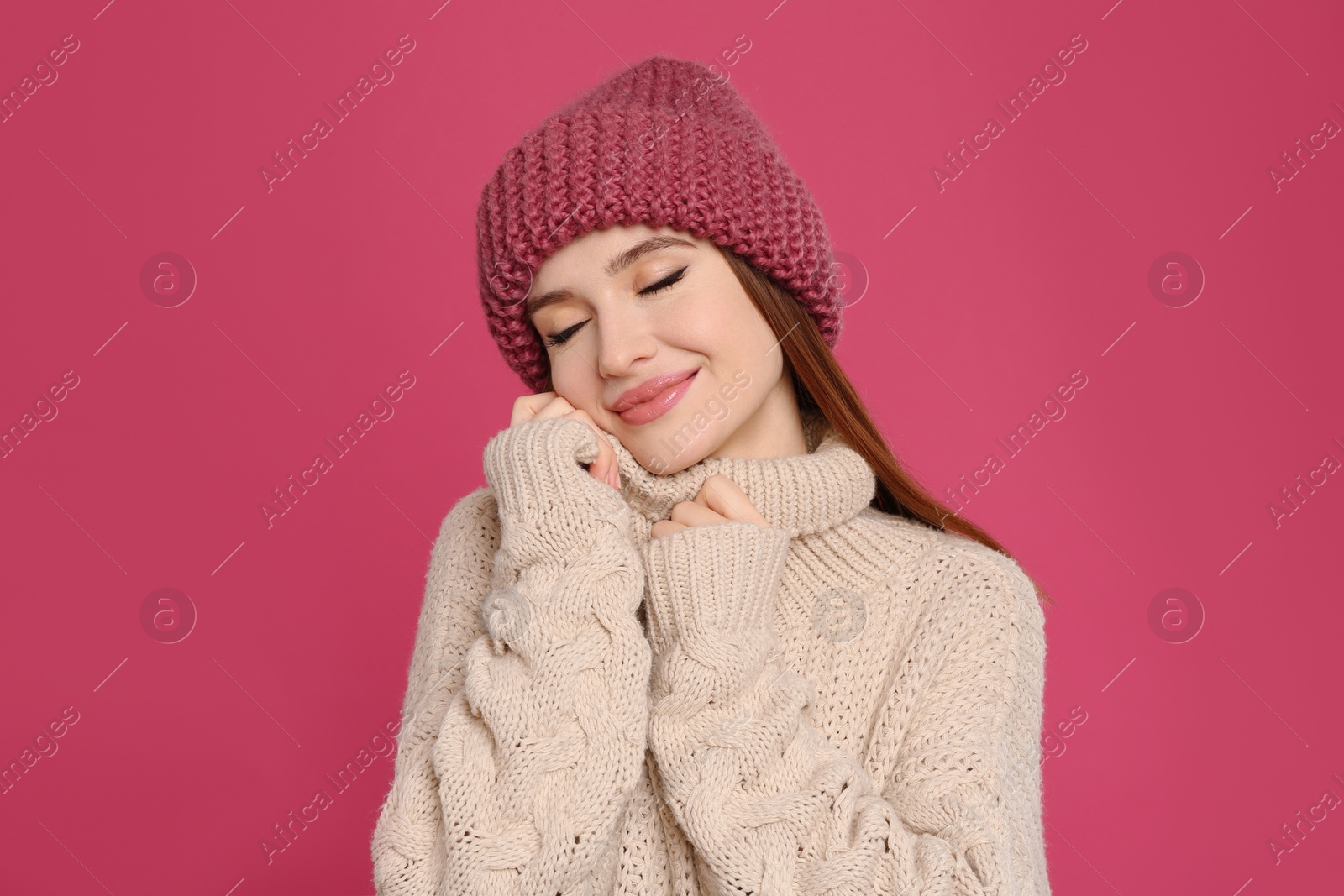 Photo of Young woman wearing warm sweater and hat on crimson background. Winter season