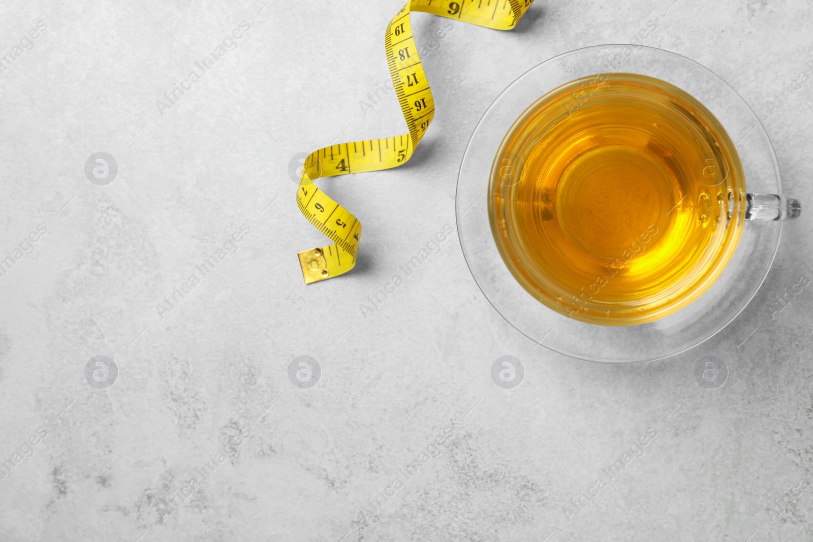 Photo of Cup of herbal diet tea and measuring tape on white table, flat lay with space for text. Weight loss concept