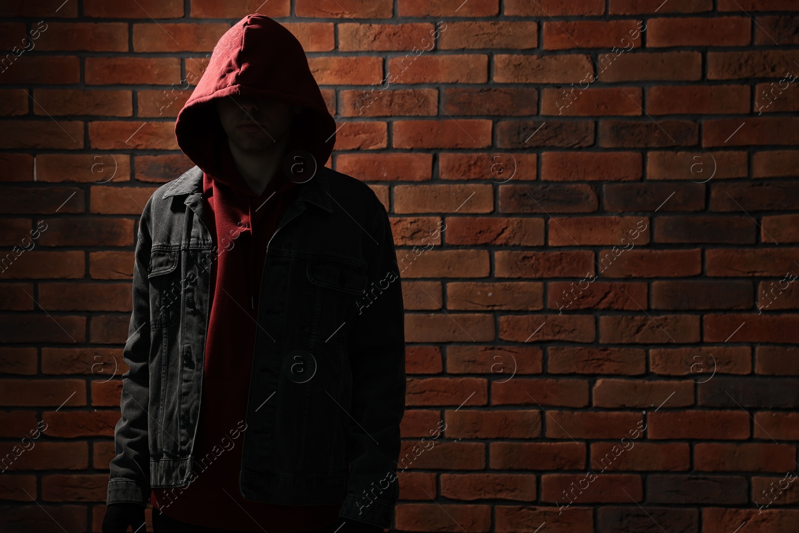 Photo of Thief in hoodie against red brick wall. Space for text