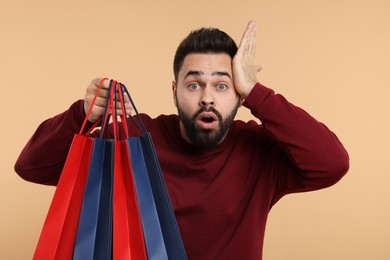 Shocked man with many paper shopping bags on beige background