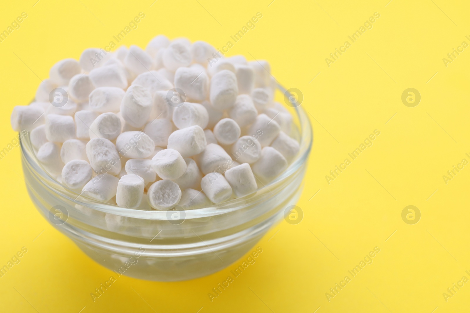 Photo of Glass bowl with delicious marshmallows on yellow background, closeup