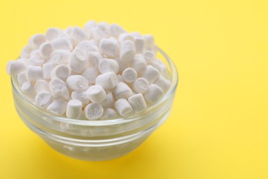 Photo of Glass bowl with delicious marshmallows on yellow background, closeup