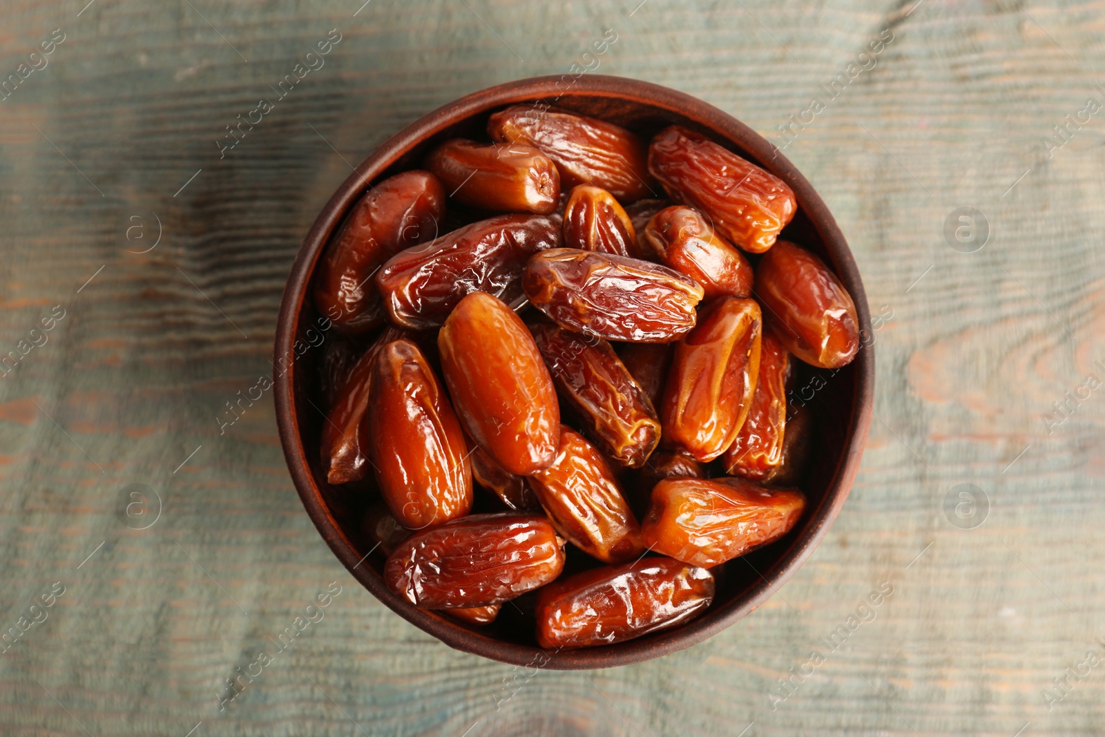 Photo of Sweet dried dates in bowl on light blue wooden table, top view