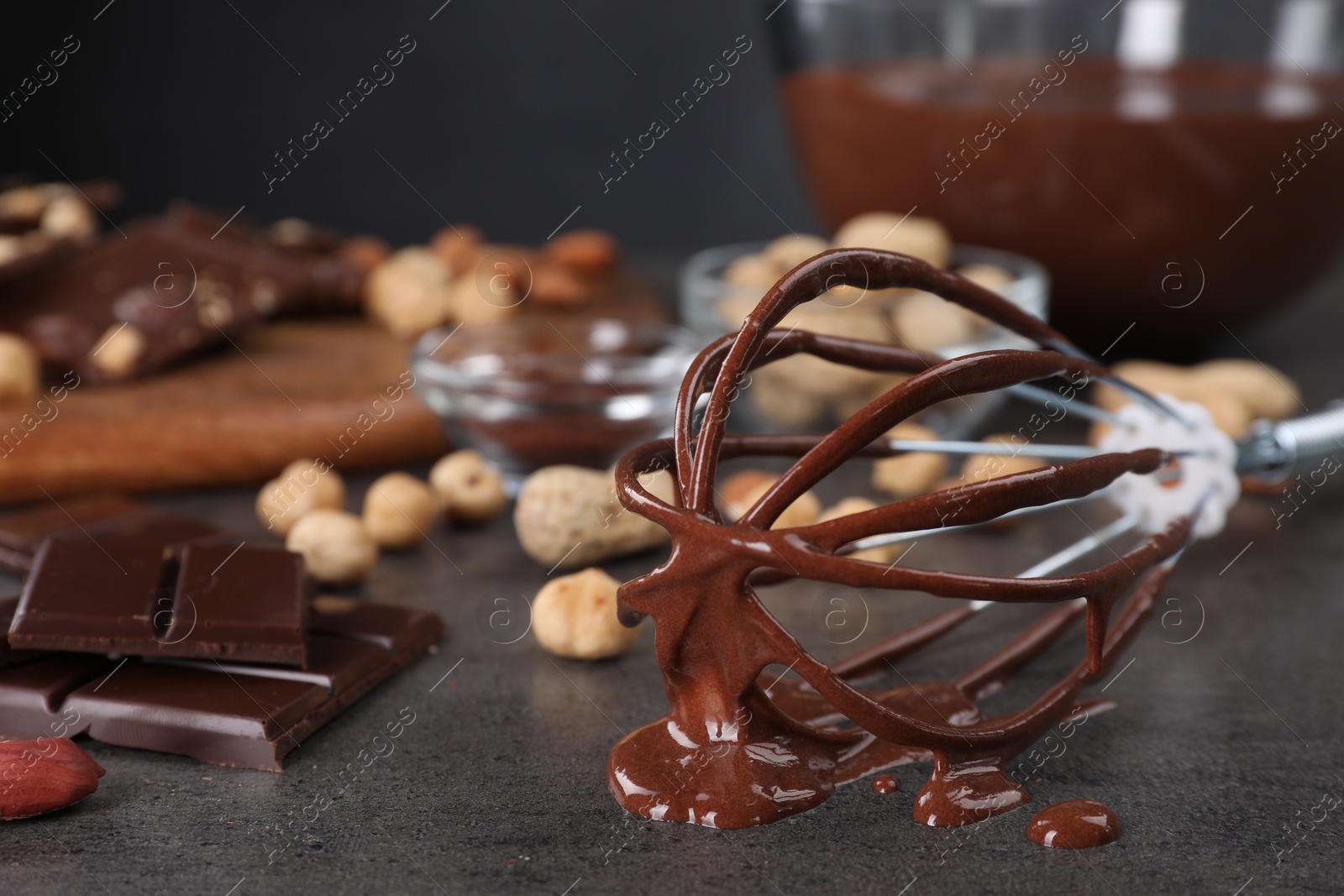 Photo of Whisk with chocolate cream and ingredients on gray table, closeup