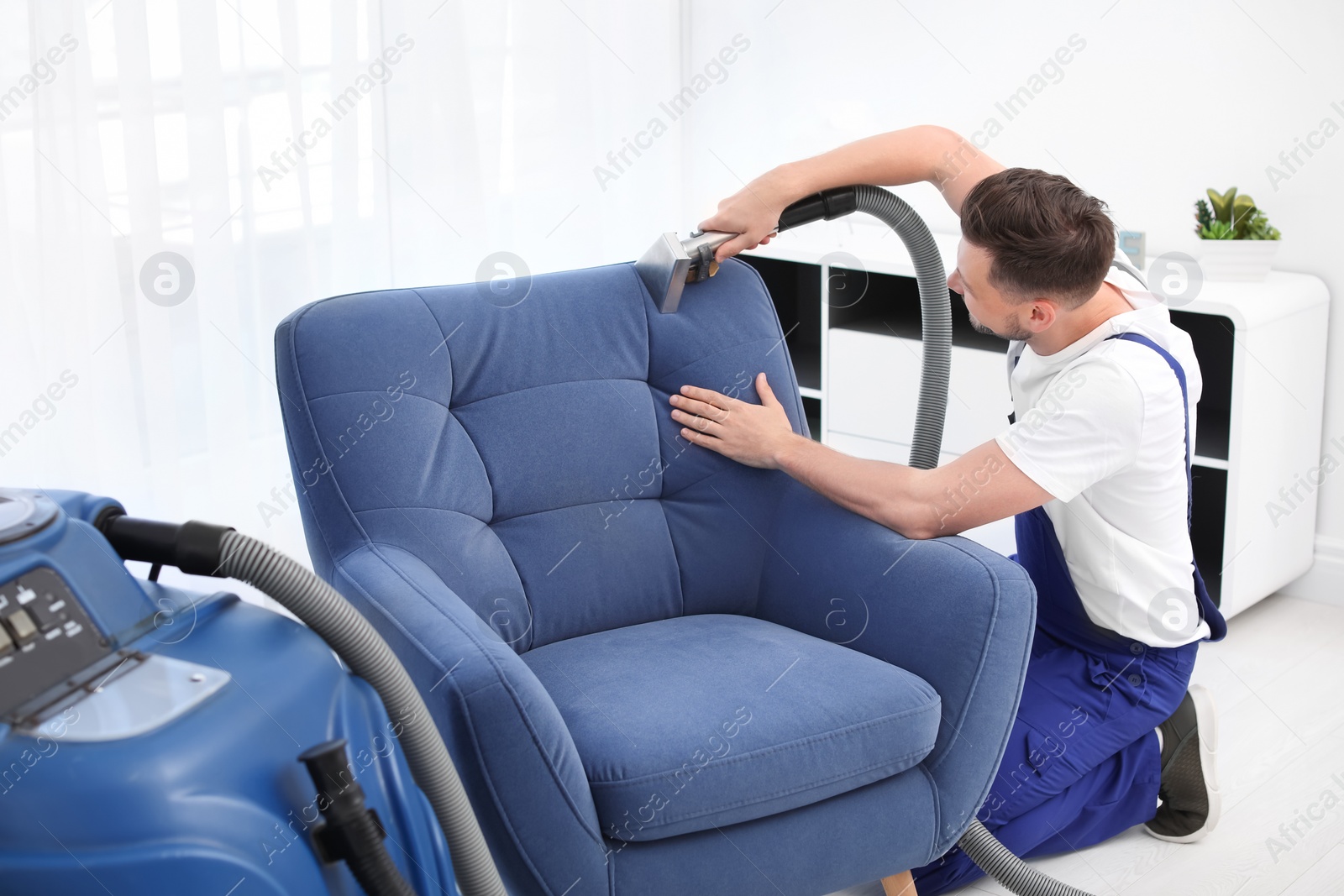 Photo of Dry cleaning worker removing dirt from armchair indoors