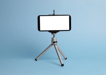 Photo of Modern tripod with smartphone on light blue background