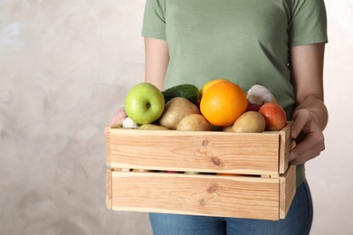 Woman holding wooden crate with fruits and vegetables on color background, closeup