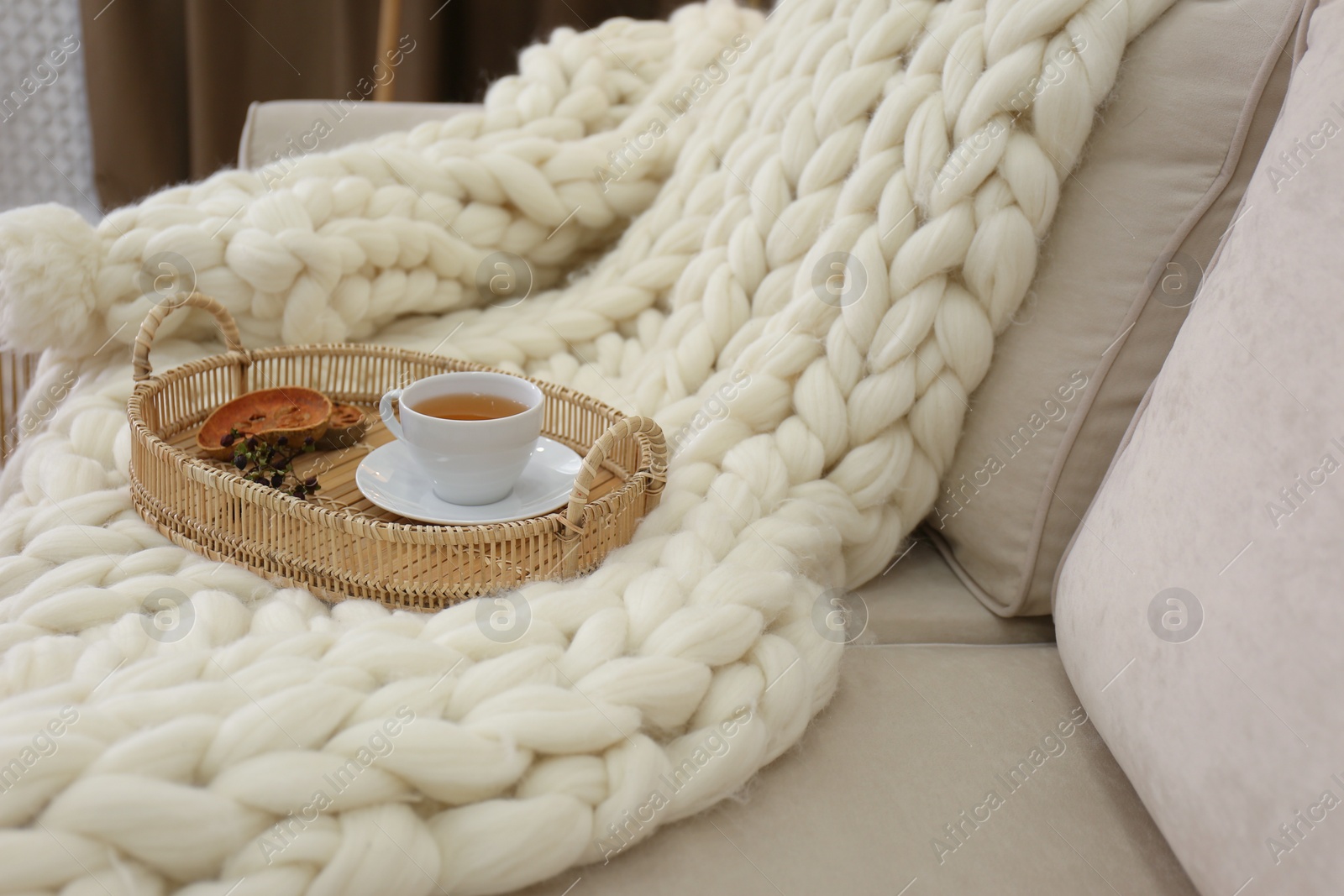 Photo of Tray with cup of tea on white knitted blanket in room. Interior element