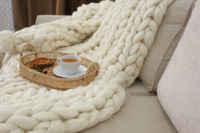 Photo of Tray with cup of tea on white knitted blanket in room. Interior element