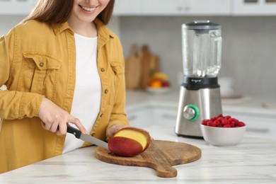 Photo of Woman preparing mango for tasty smoothie at white marble table in kitchen, closeup