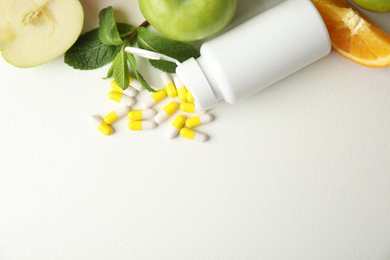 Bottle with vitamin pills and fruits on white table, flat lay. Space for text