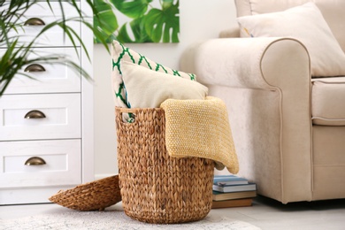 Photo of Basket with soft plaid and pillows in living room interior