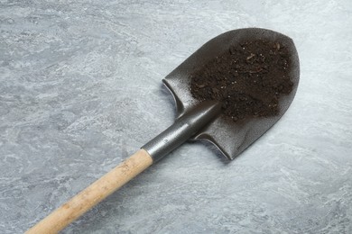 Photo of Metal shovel with fertile soil on gray textured surface, above view