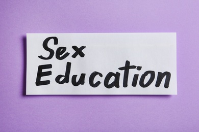 Photo of Piece of paper with phrase "SEX EDUCATION" on violet background, top view