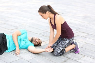 Photo of Woman checking pulse of unconscious man outdoors