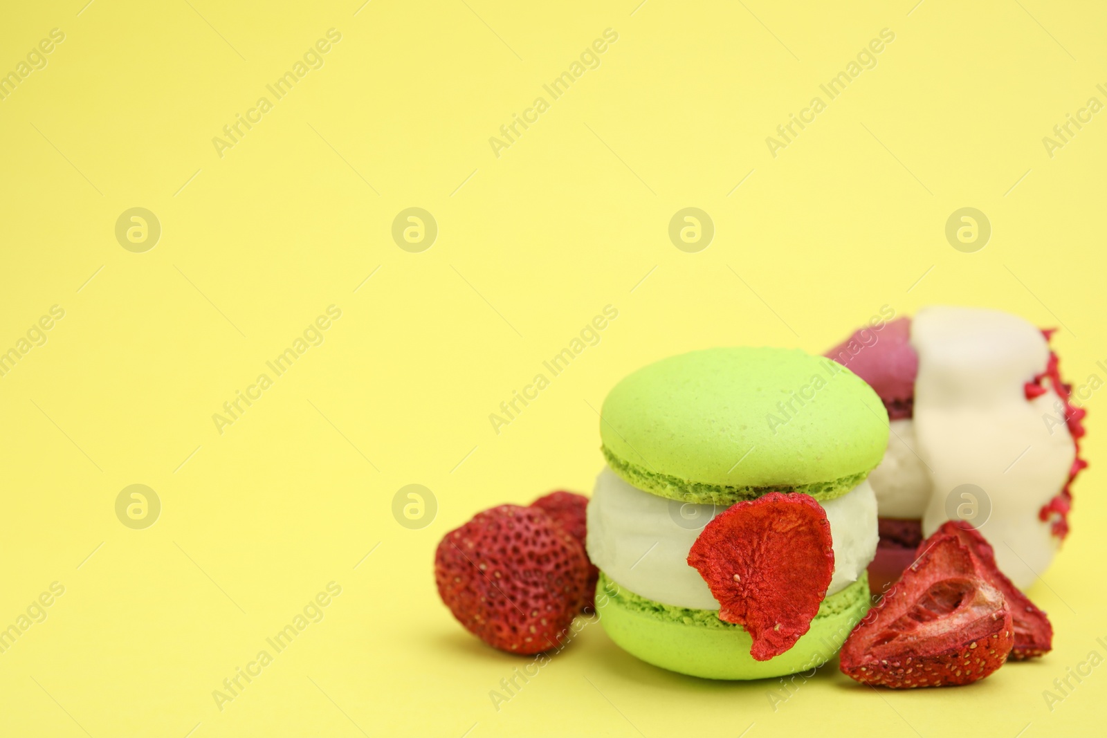 Photo of Delicious macarons and dry strawberries on yellow background, closeup. Space for text