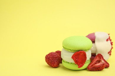 Delicious macarons and dry strawberries on yellow background, closeup. Space for text