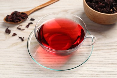 Photo of Cup of fresh hibiscus tea and dry flower leaves on wooden table