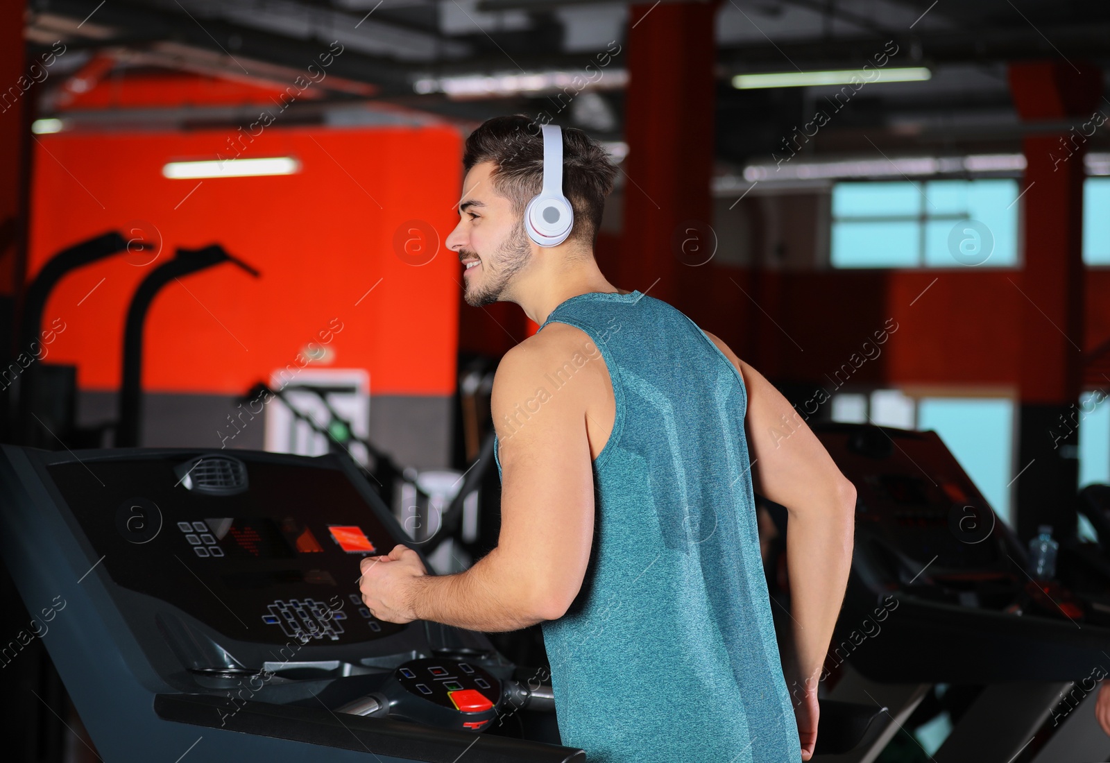 Photo of Young man with headphones listening to music and running on treadmill at gym