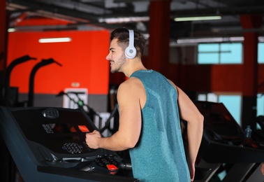 Photo of Young man with headphones listening to music and running on treadmill at gym