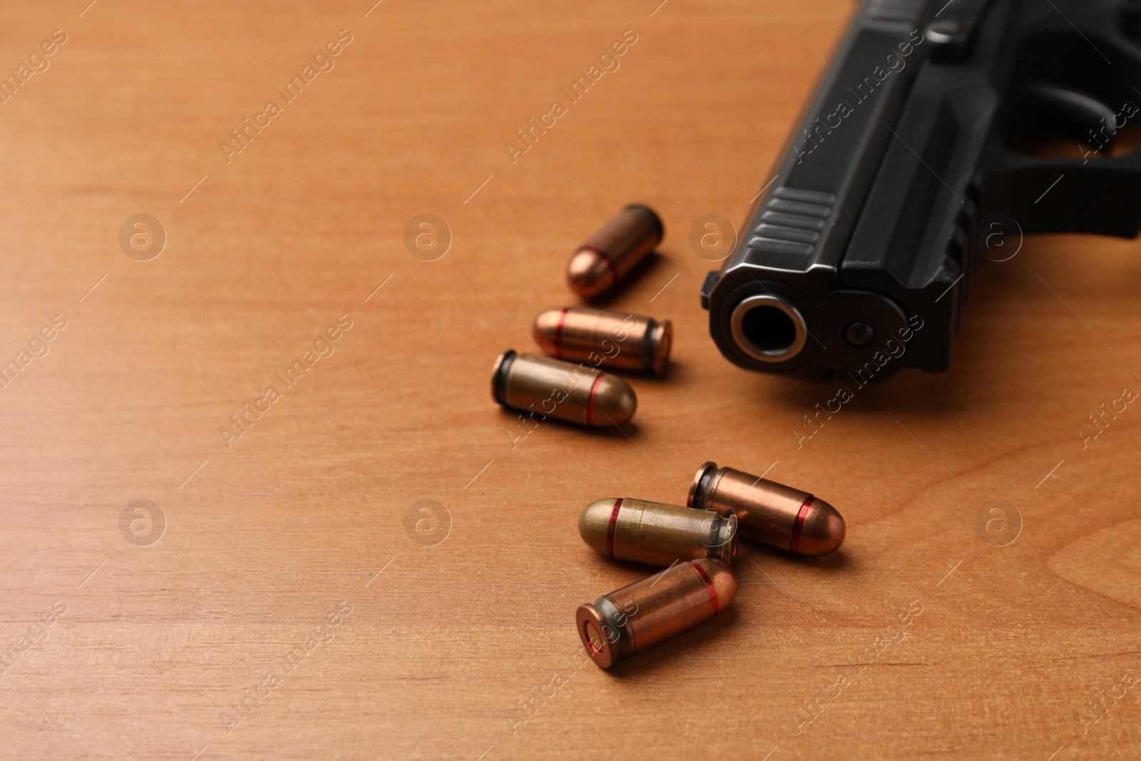 Photo of Semi-automatic pistol and bullets on wooden table, closeup. Space for text