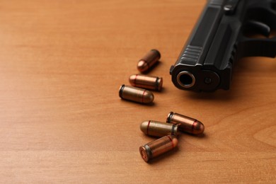 Photo of Semi-automatic pistol and bullets on wooden table, closeup. Space for text