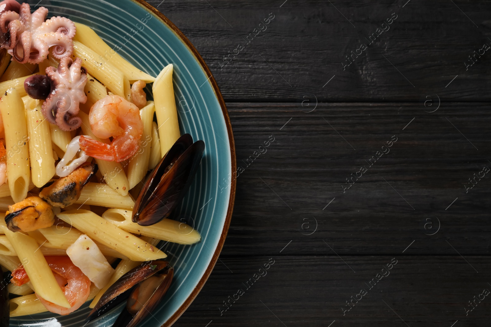 Photo of Delicious pasta with seafood served on black wooden table, top view. Space for text